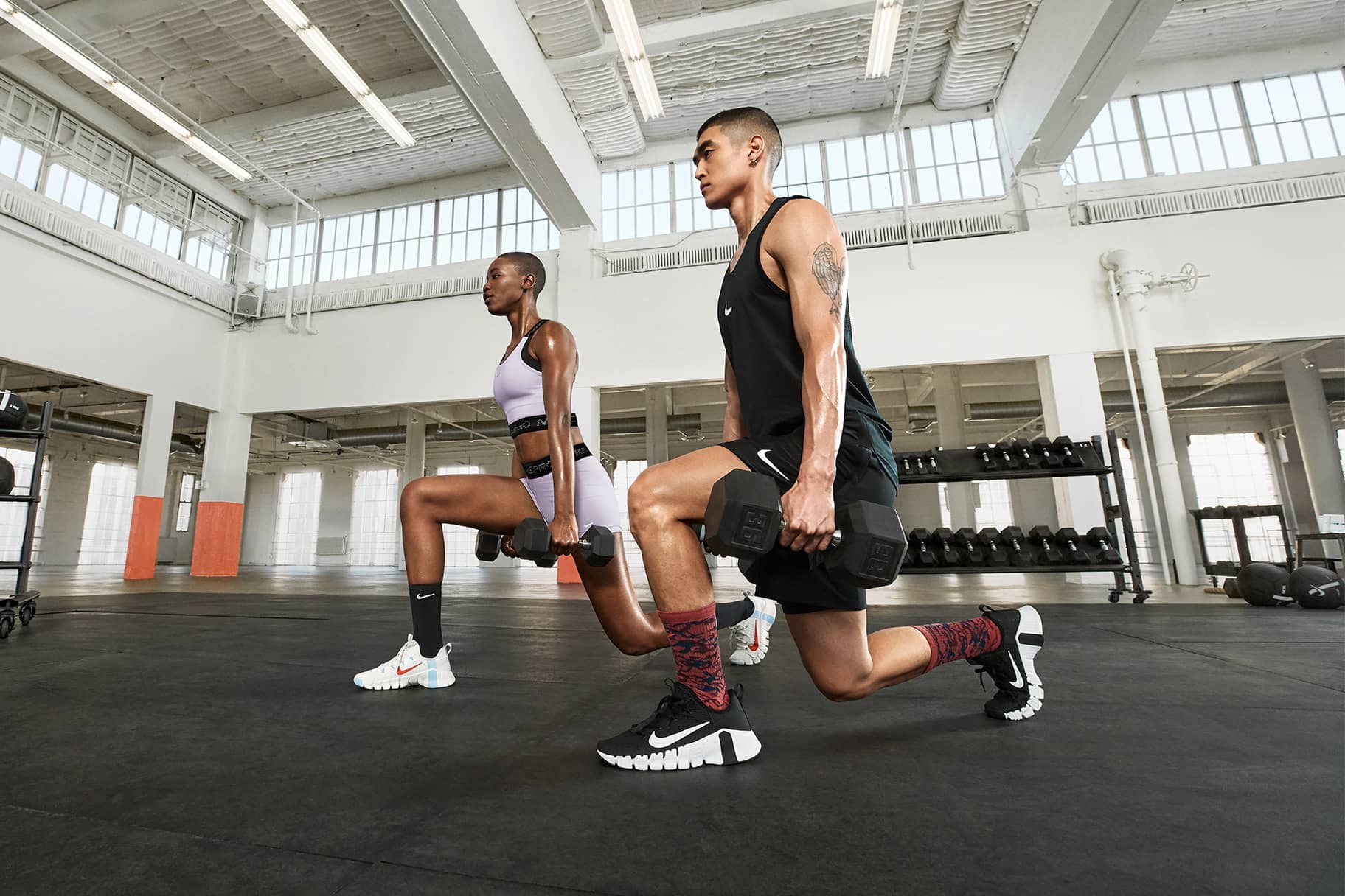 Two athletes performing weighted lunges in a gym