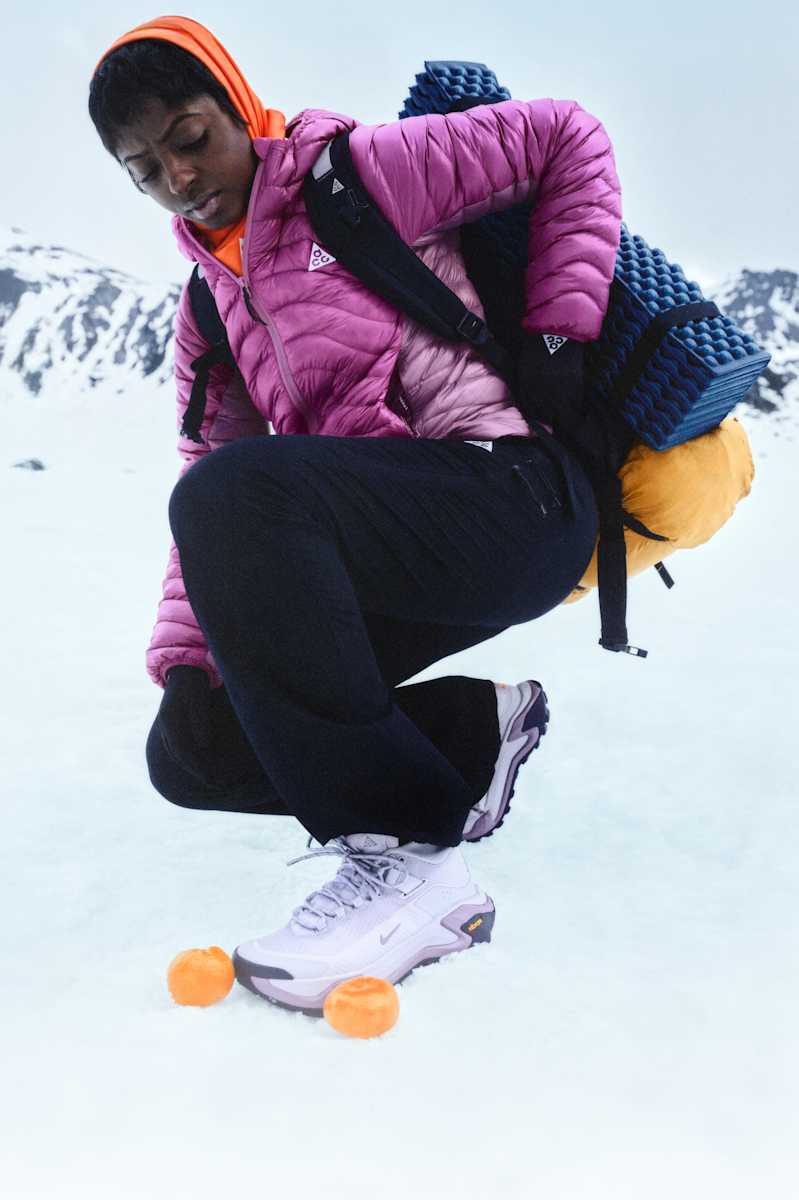 Eine Person mit schwerem gelbem Rucksack trägt in einer verschneiten Umgebung eine lila Nike ACG Puffer-Jacke., Dein Schutzschild gegen Wind und Regen