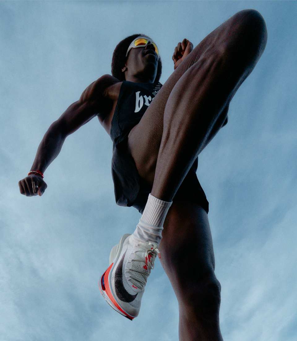 Zwart Nike Aeroswift-hemd met witte Nike Alphafly 4-sneakers, van onderaf gefotografeerd tijdens het hardlopen.