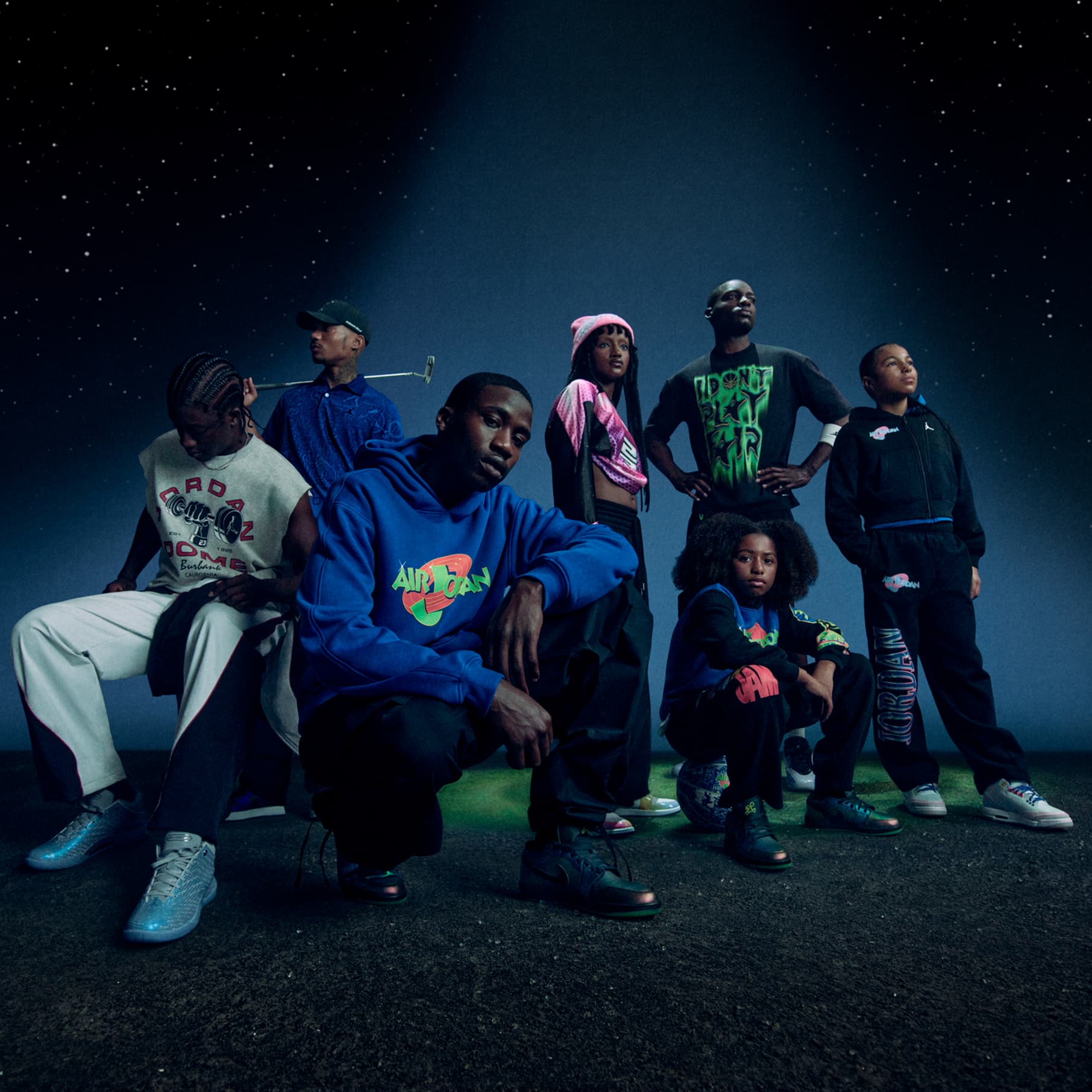 Syv personer poserer under et spotlys med en stjerneklar nattehimmel som baggrund iført farverigt Jordan x Space Jam-tøj. Jordan Jumpman- og Space Jam-logoerne vises i venstre side af billedet., JORDAN BRAND x SPACE JAM