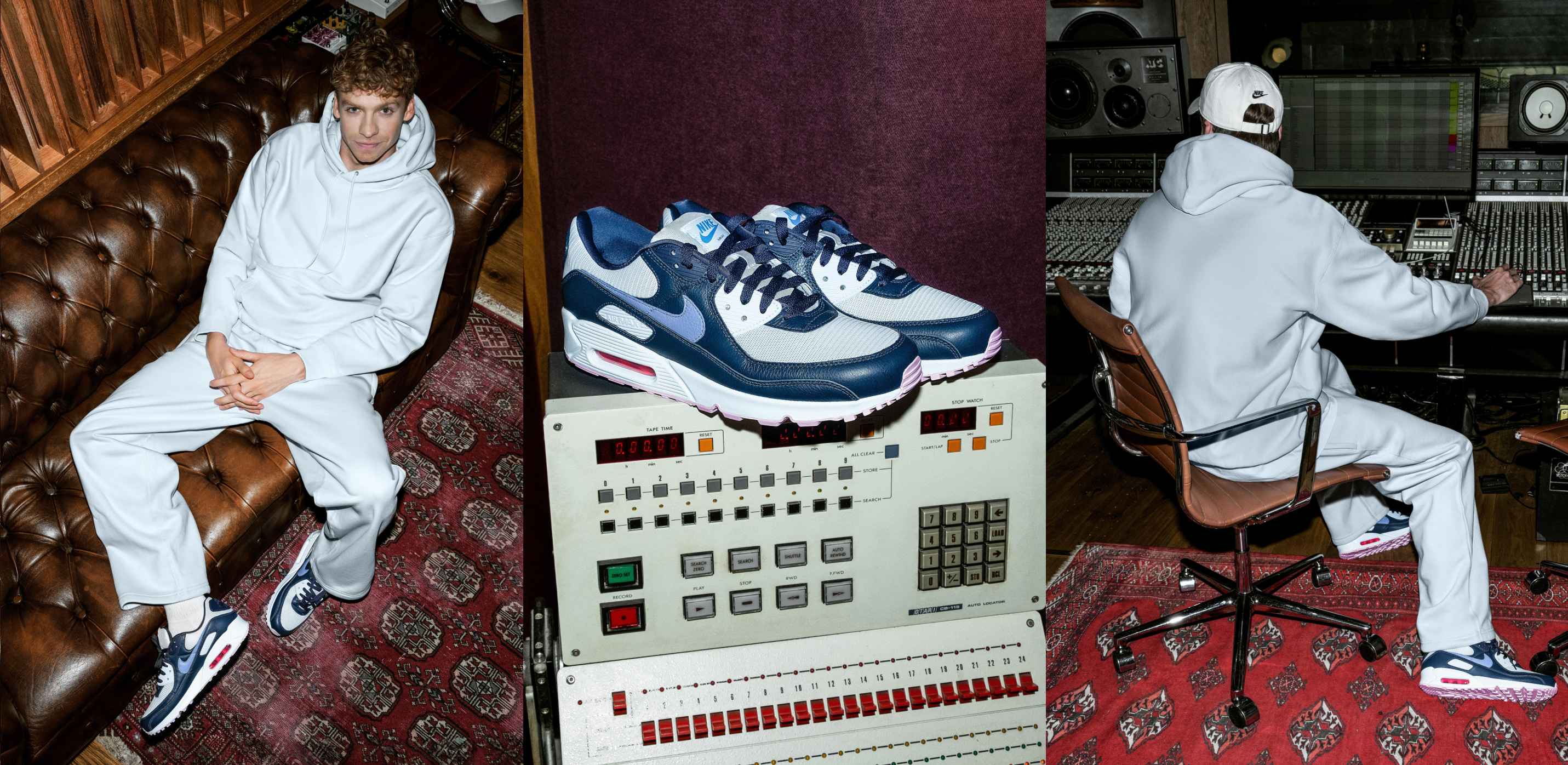 A man sitting on a brown leather sofa, wearing a light blue hoodie and trousers, and dark blue and white Nike Air Max 90s.