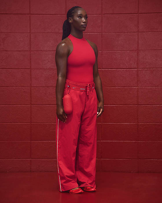 Athlete wears bright red NikeSKIMS top and pants, with red NikeSKIMS Rift, against a red wall., slide 1 of 5