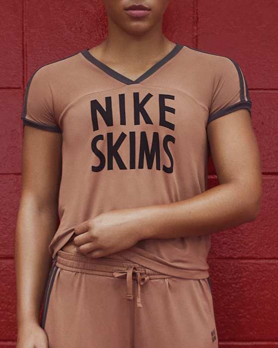 Eine Athletin trägt ein braunes NikeSKIMS-Oberteil und -Shorts mit dunkelbraunen Einfassungen an Armen und Ausschnitt., slide 4 of 5