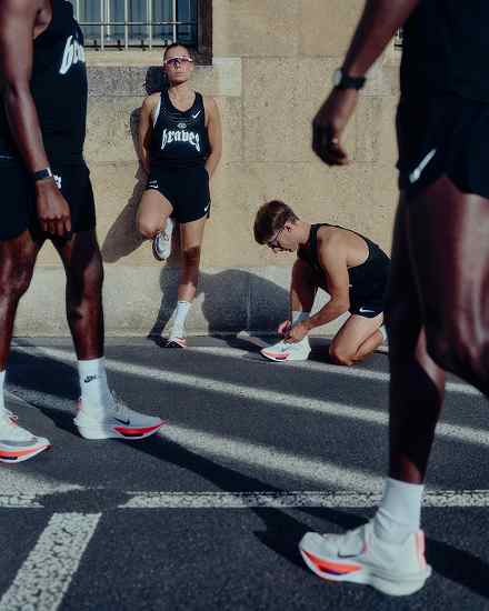 Groupe de coureurs portant des débardeurs et des shorts Nike Aeroswift noirs et des chaussures de running Nike Alphafly 4 blanches, sur une route baignée de soleil., slide 3 of 3