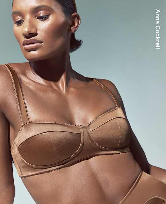 As Worn by Athletes, Anna Cockrell looking down in a studio space, wearing a brown bra and matching leggings., slide 2 of 3