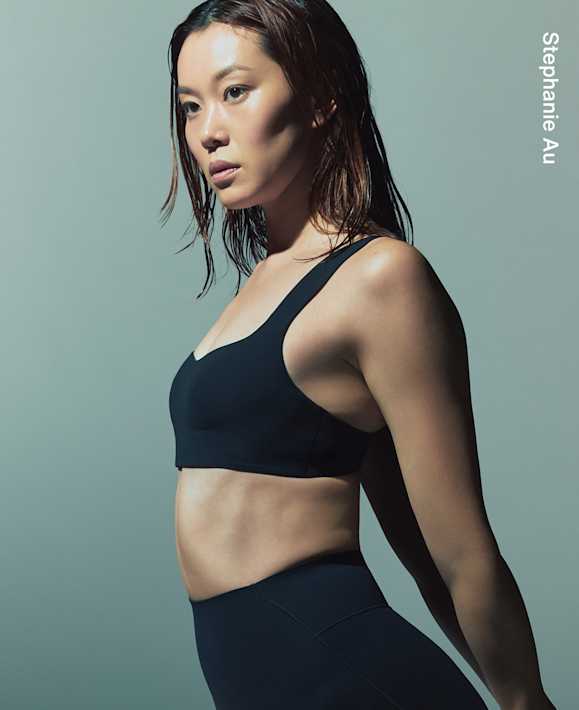 As Worn by Athletes, Stephanie Au standing with wet hair in a light grey studio, wearing a black sports bra and black leggings., slide 1 of 3