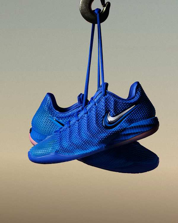 Aktuelle Trends, Ein Paar blaue Nike Caitlin 1 Schuhe, die an ihren Schnürsenkeln an einem Metallhaken vor einem Hintergrund mit Farbverlauf hängen., slide 1 of 5