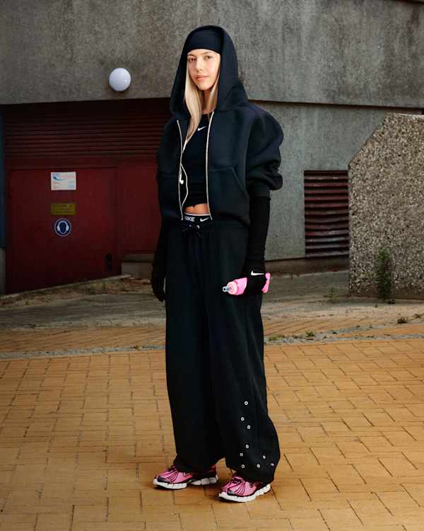 Novidades, Uma mulher no exterior a usar conjunto com capuz preto, luvas pretas, e sapatilhas Nike Zoom Skylon 11 rosa Bright e pretas, enquanto segura uma garrafa rosa., slide 2 of 5