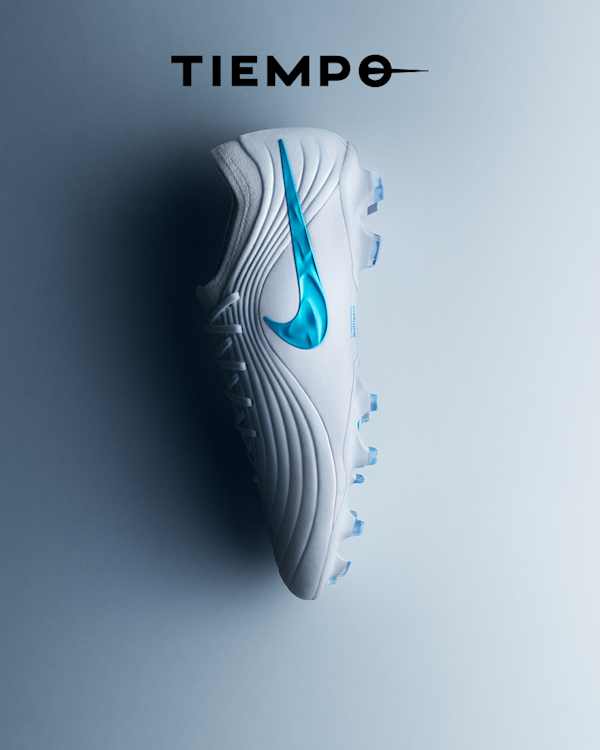 Explore the Bright Lights Pack, A white Nike Tiempo football boot lying on its side on a grey and blue gradient surface, with a blue swoosh and blue studs., slide 4 of 4