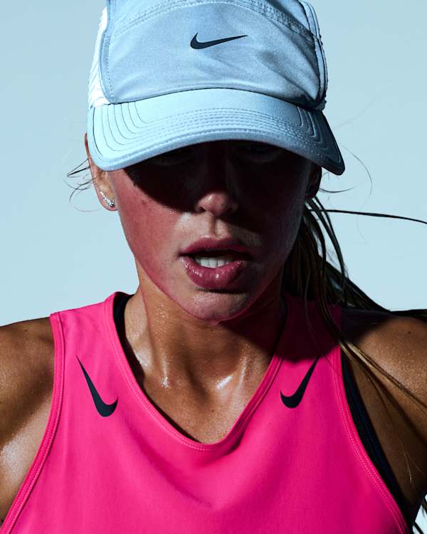 Shop Running, A woman running in a bright setting, wearing a light grey Nike cap and a pink Nike vest., slide 3 of 3