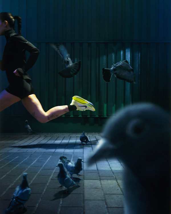 Il y a du nouveau, Une femme court sur une rue pavée sombre où se trouvent des pigeons. Elle porte un haut noir, un short noir et des chaussures de running Nike jaunes., slide 2 of 5