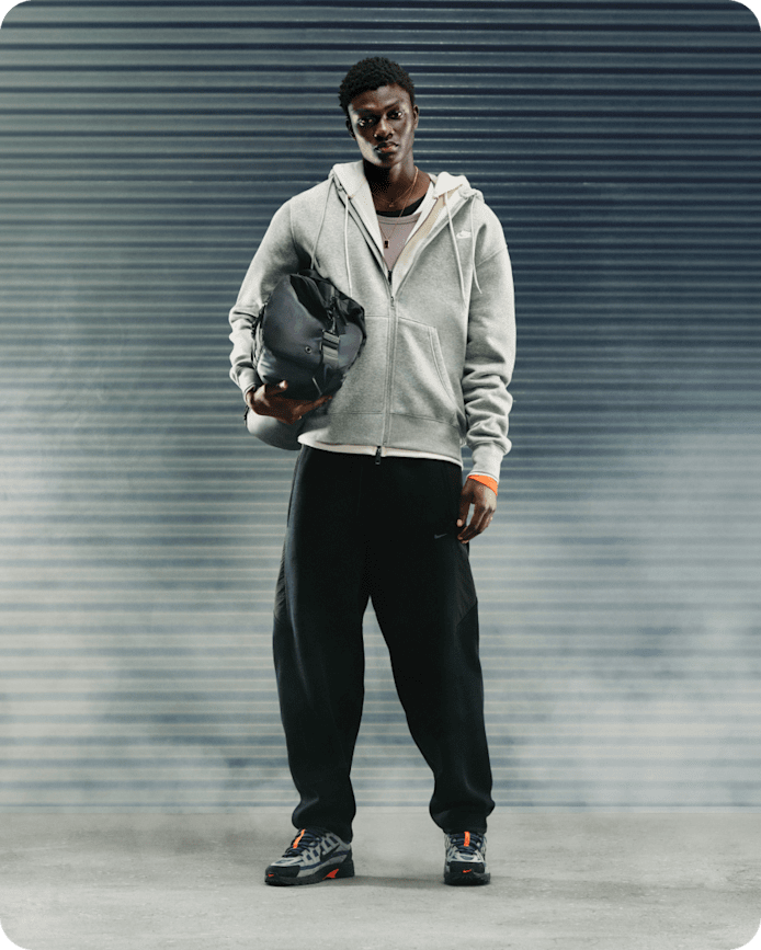 Mehr Inspo für deine Nike Sportswear Looks, Ein Mann steht an einer grauen Wand, hält eine schwarze Tasche in der Hand und trägt einen grauen Hoodie, eine schwarze Hose und den Nike P-6000 in Grau und Schwarz., slide 1 of 5
