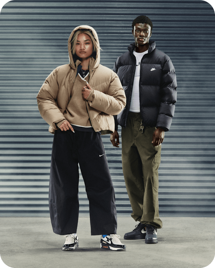 Plus d'idées de looks Nike Sportswear, Une femme et un homme debout dans un espace gris. Elle porte une doudoune beige, un pantalon noir et des Air Max 90. Il porte une doudoune noire, un pantalon olive et des Air Force 1 noires., slide 5 of 5