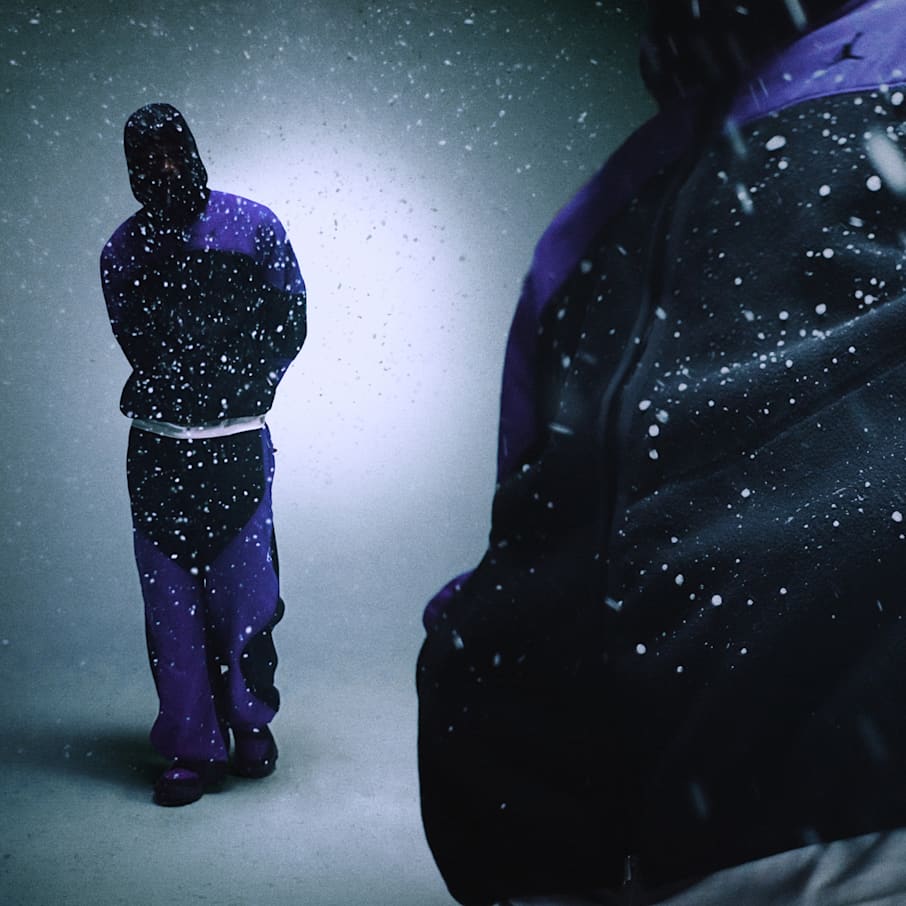 Una persona sotto la neve che indossa una tuta Jordan in fleece nera e viola, con un primo piano del tessuto fleece testurizzato in primo piano., STAY DRY. STAY WARM. STAY READY.