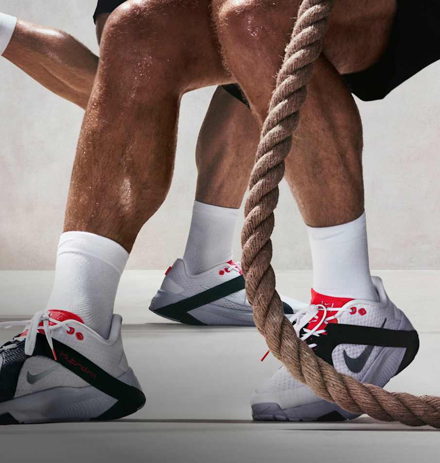 To menn som sitter på huk i et treningsstudio, holder et tykt tau og har på seg hvite sokker og Nike Hybrid RN-treningssko., Hybridsko