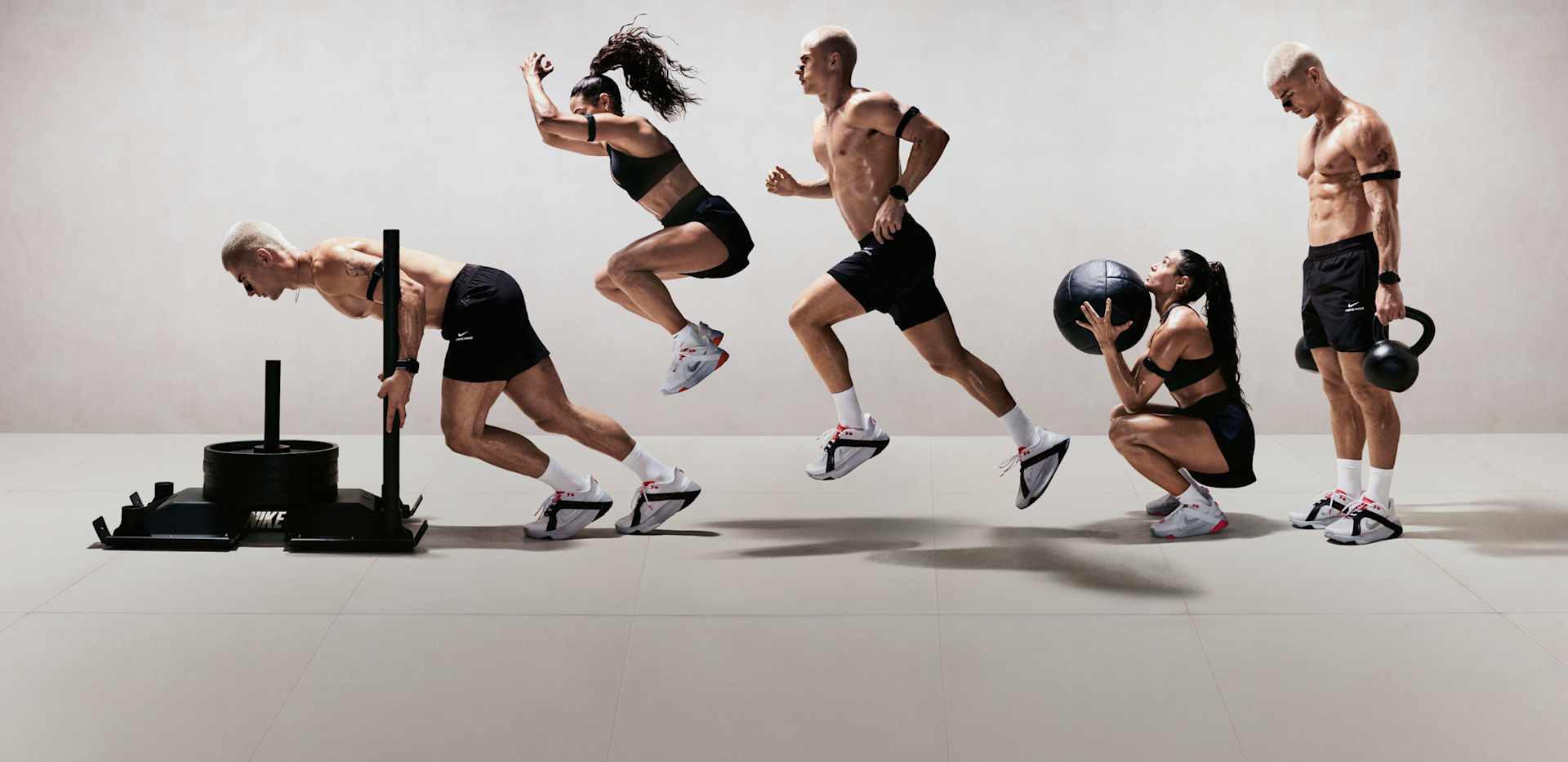 Un uomo e una donna eseguono vari esercizi di forza e preparazione fisica in uno spazio luminoso, indossando abbigliamento da allenamento nero e scarpe da training Nike Hybrid RN., ALLENATI SENZA LIMITI