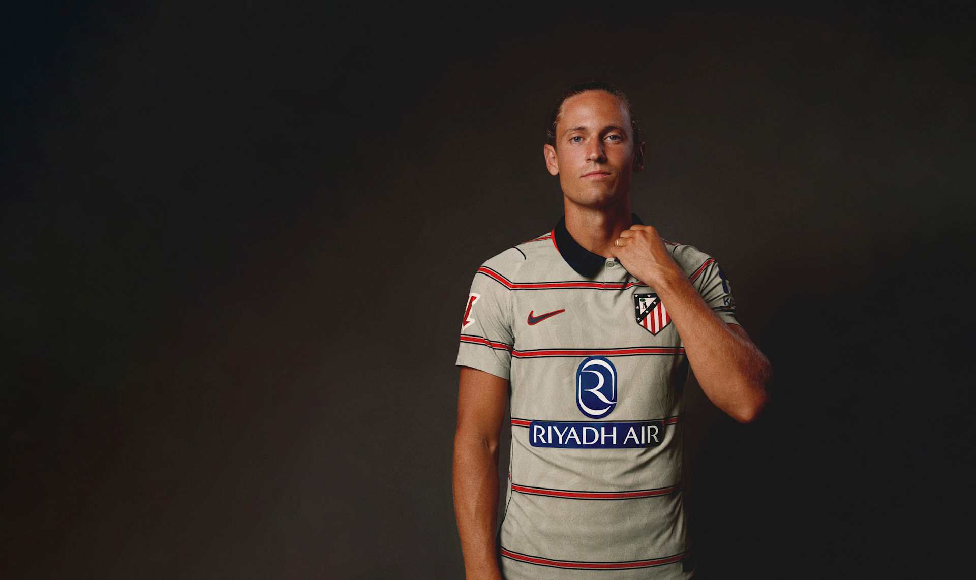 A white football shirt floating against a dark gradient background, with red stripes, a blue collar, Nike branding, and club crest., WEAR WHAT<br>YOU STAND FOR