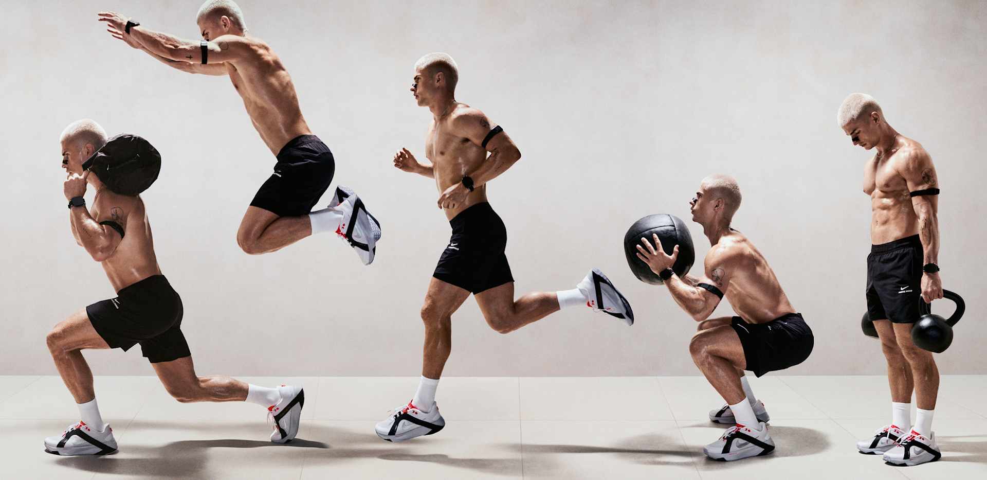 Un hombre realiza varios ejercicios de fuerza y agilidad en un estudio gris. Lleva pantalones cortos negros y zapatillas de entrenamiento Nike Hybrid RN., ENTRENA SIN LÍMITES