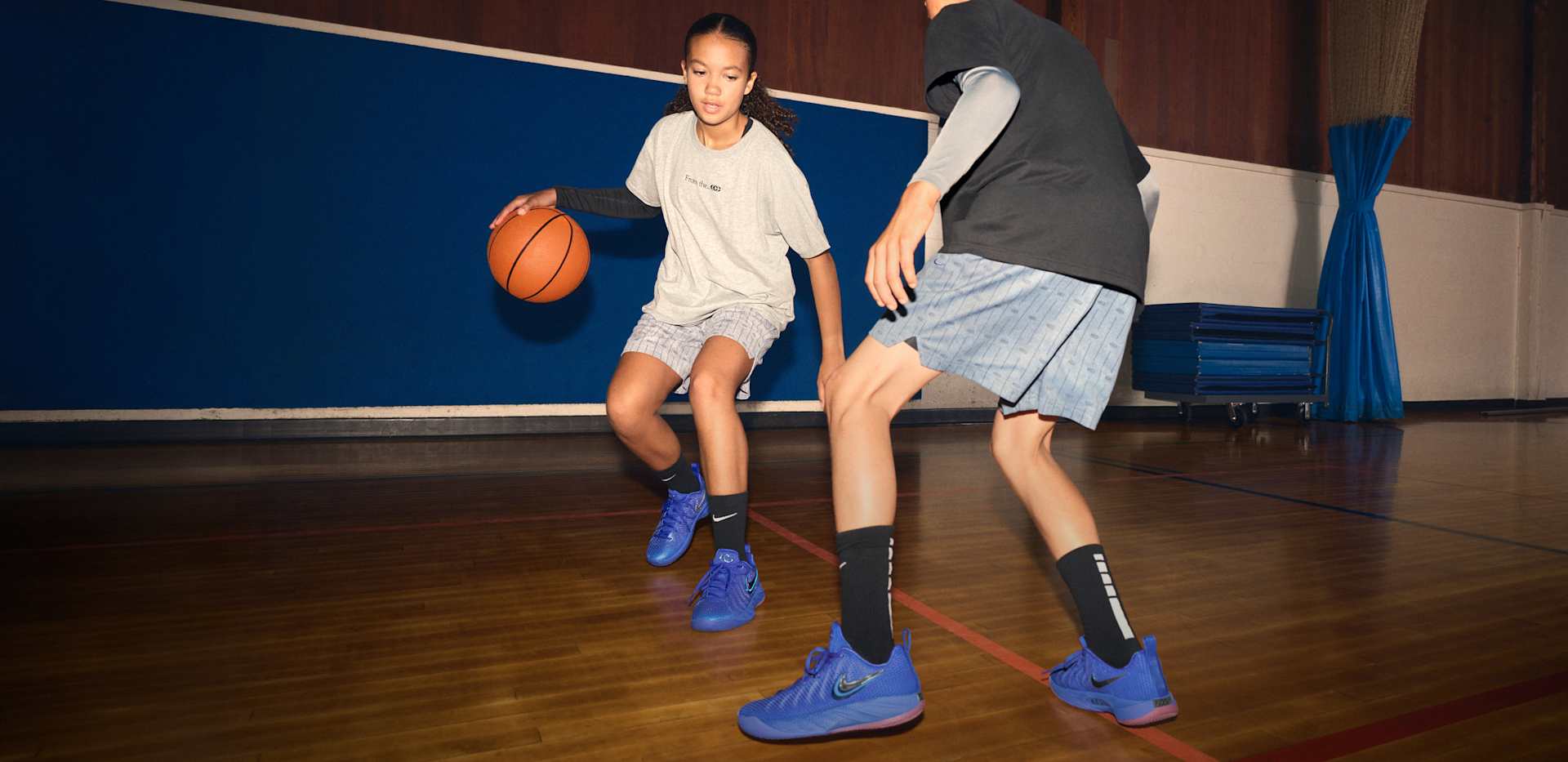 Two young basketballers play on a hardwood court, each wearing Caitlin 1 shoes and apparel., CAITLIN 1