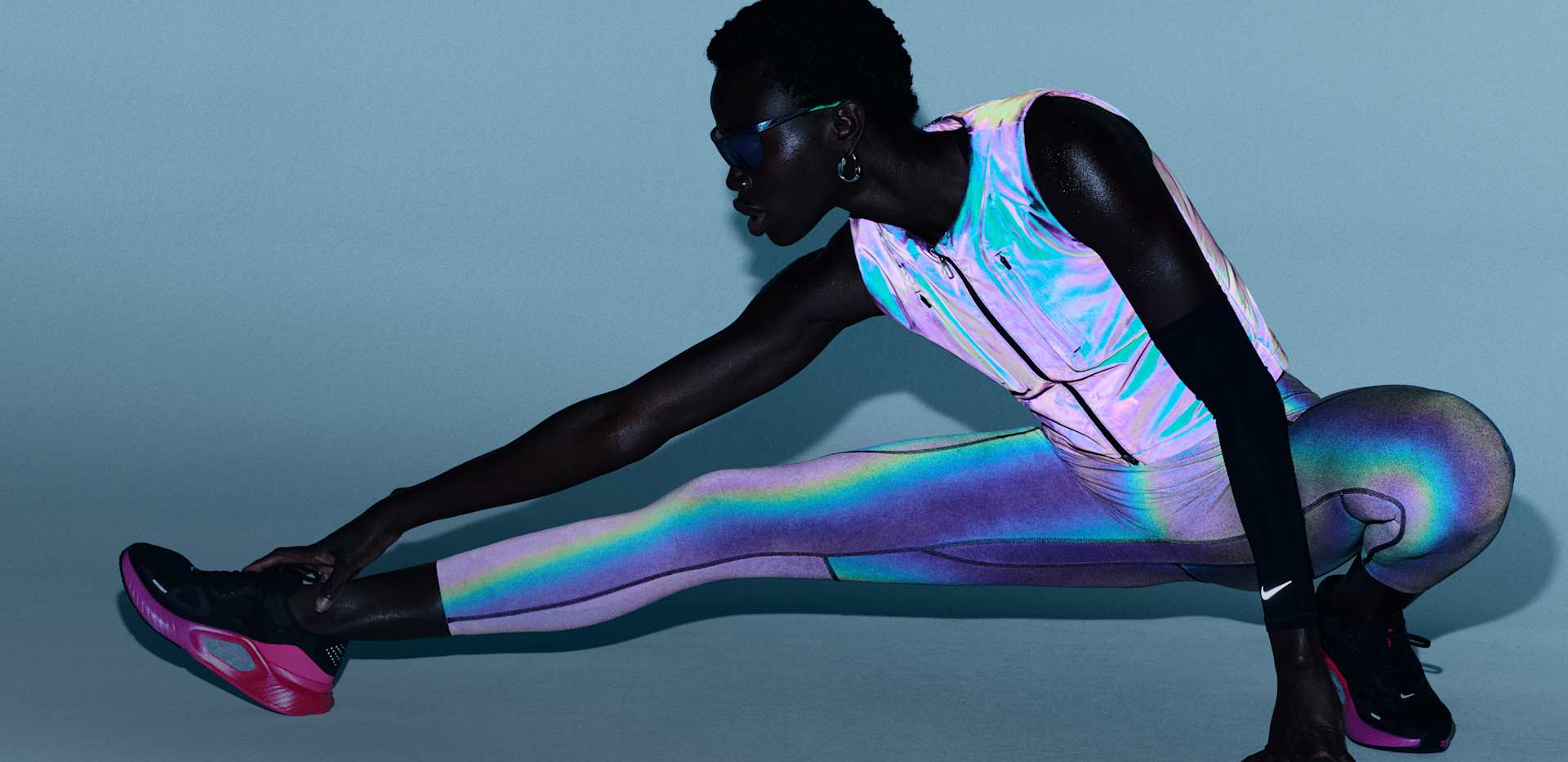 Una donna che si allunga in avanti su uno sfondo blu, indossando uno smanicato da running rifrangente, leggings coordinati, manicotti neri e scarpe Nike Structure nere e rosa. , FATTI NOTARE FIN DALL'INIZIO