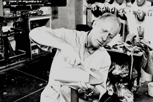Black-and-white portrait of Bill Boweman tinkering with a shoe in a workshop, slide 3 of 10
