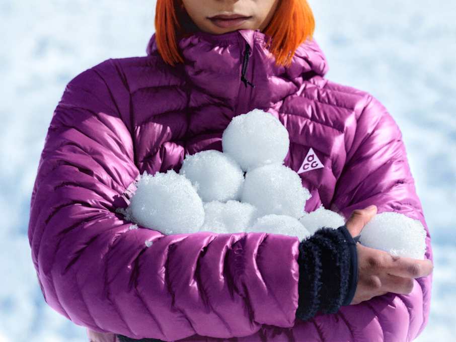Grande plano de uma pessoa com um casaco almofadado ACG roxo que segura várias bolas de neve., Descobre a série ACG Lava
