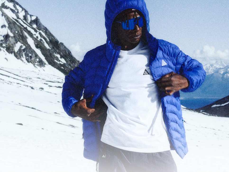 Uma pessoa na neve com casaco almofadado com capuz Nike ACG em azul Bright e primeira camada Nike ACG branca., Primeira camada, mas não básica