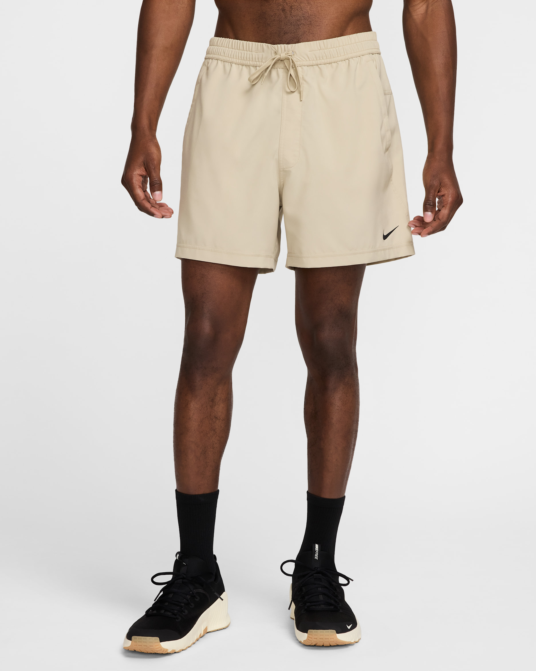Beige woven training shorts with a drawcord waist and room around the thighs