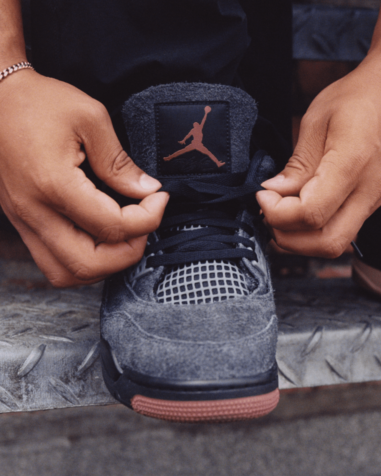Een man strikt zijn veter op een metalen trede. Hij draagt grijze Jordan 4 schoenen met een rood Jumpman logo.