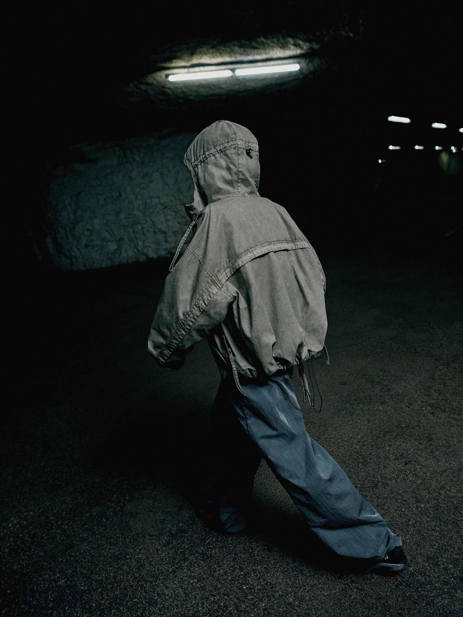 A model in a gray jacket walks through a dark, industrial interior.