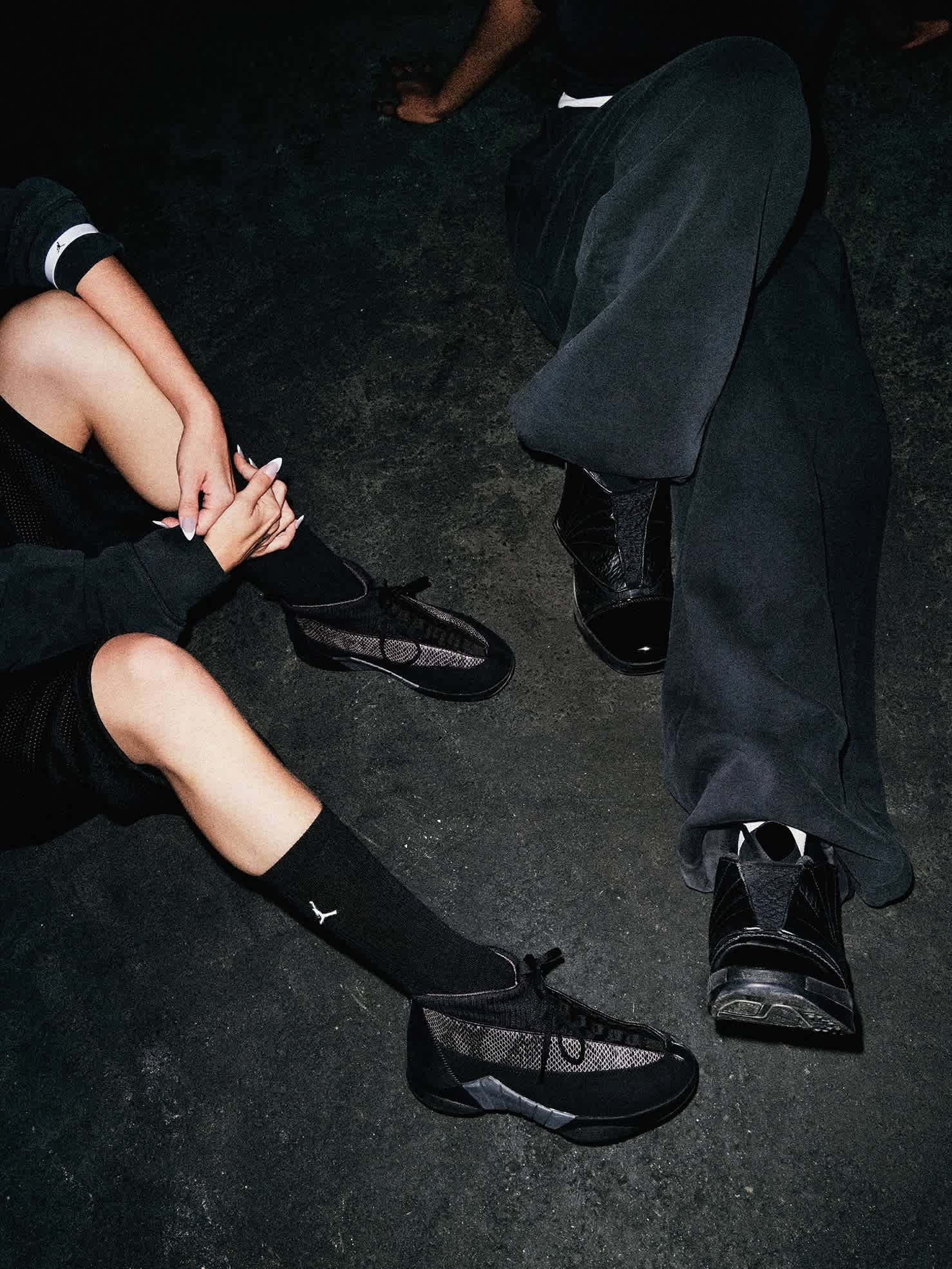 Close-up photo pointing towards the ground, showing two pairs of feet wearing black Jordan Brand shoes.