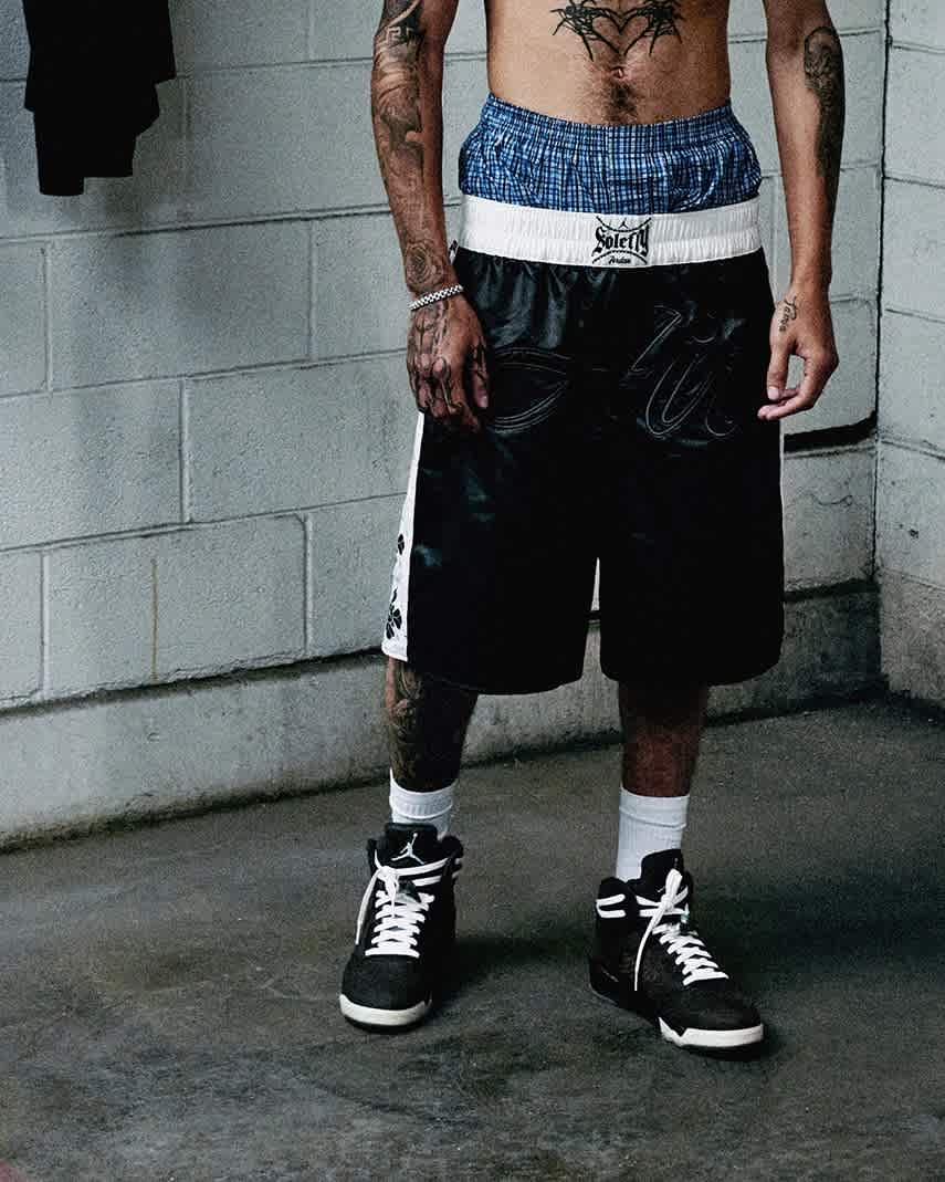 A cropped in photo of a model wearing black basketball shorts and black Jordan shoes, inside a concrete space.