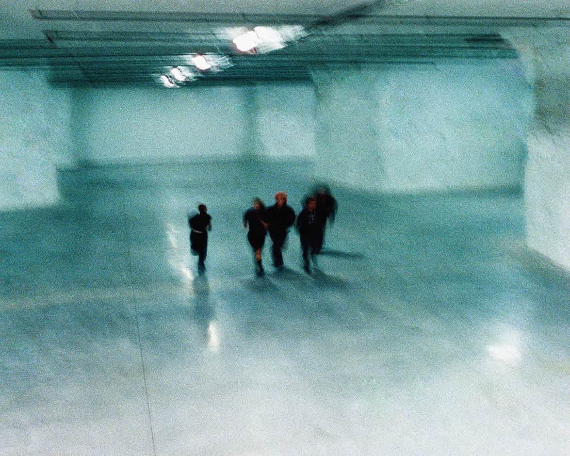 Five silhouetted figures walk through a blurry cave-like area.