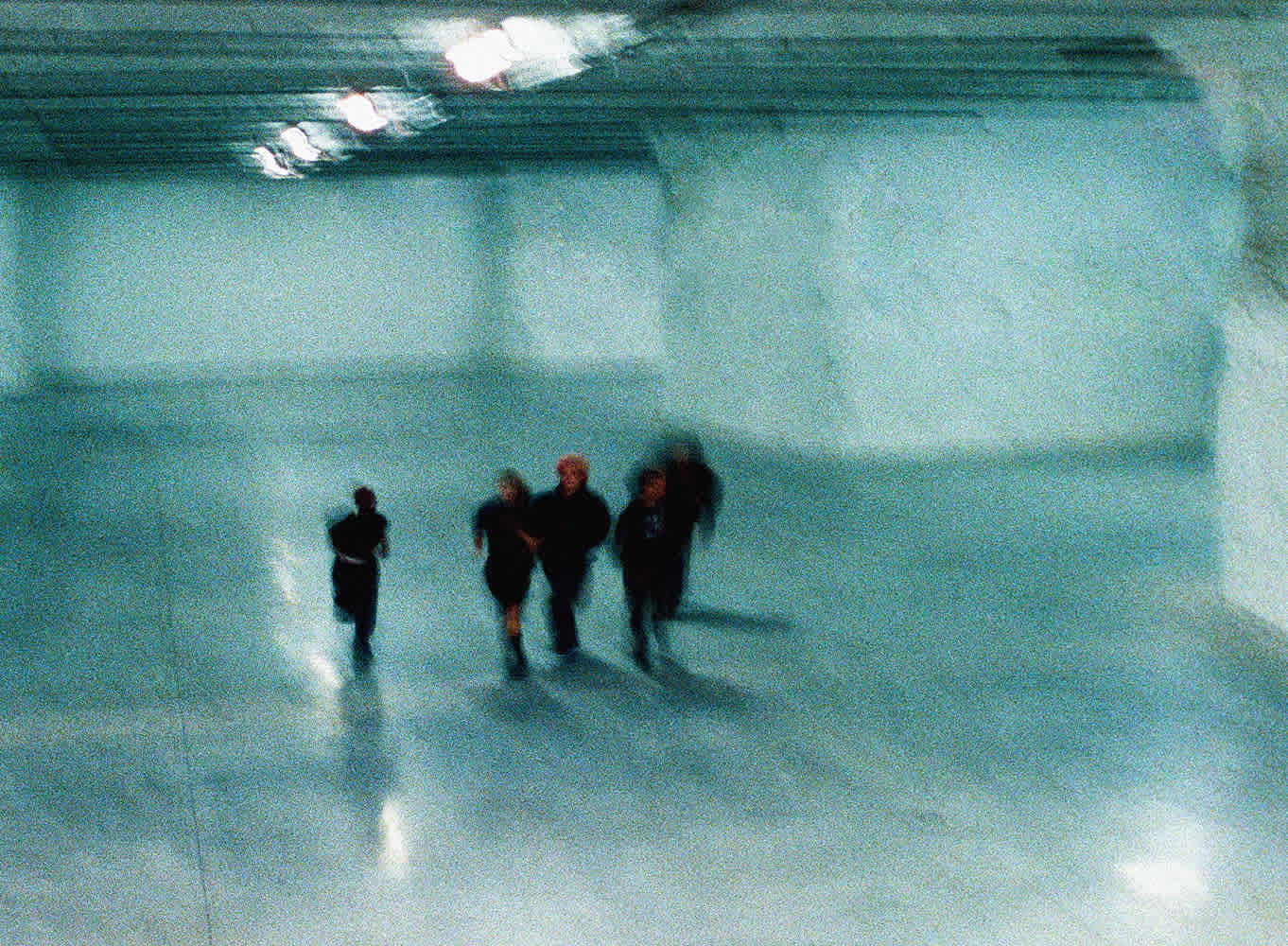 Five silhouetted figures walk through a blurry cave-like area.