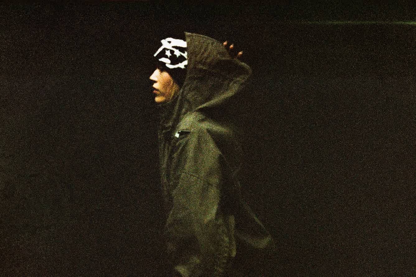 A side profile view of a female model wearing a graphic beanie and a hooded jacket.