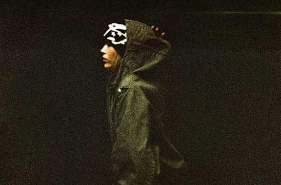 A side profile view of a female model wearing a graphic beanie and a hooded jacket.